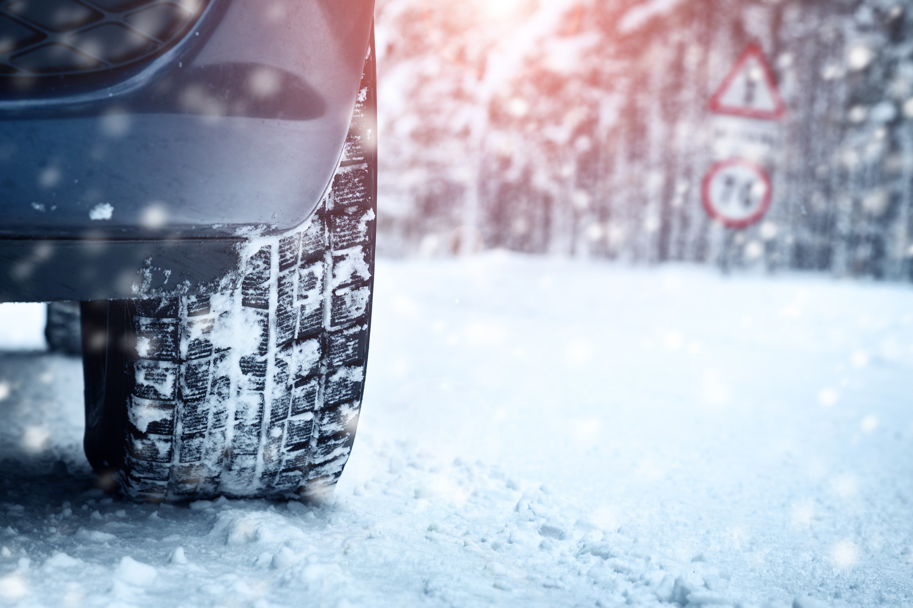 Close-up of a car tire gripping a snowy road near winter warning signs.